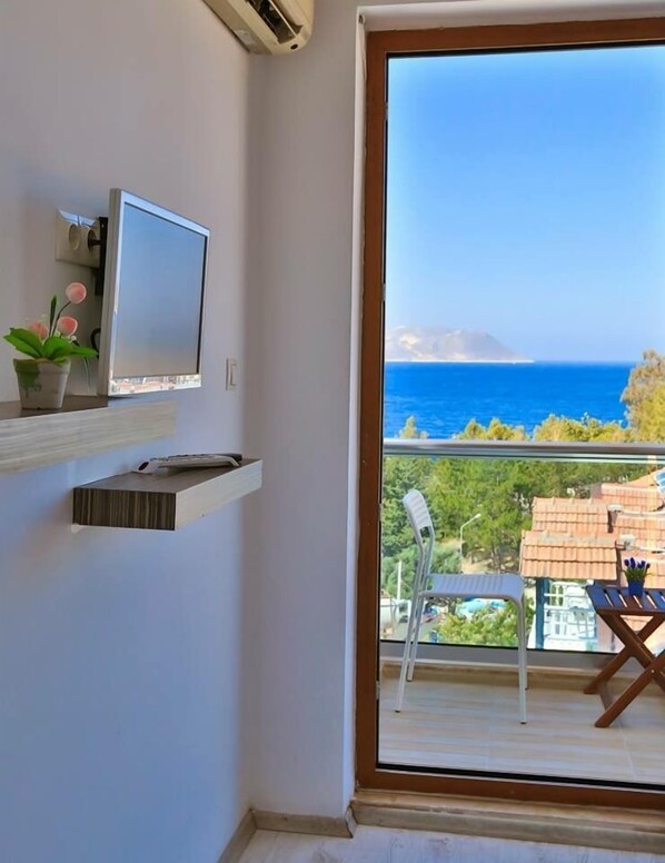 A balcony with a view of the sea, a TV on a shelf, and a chair.