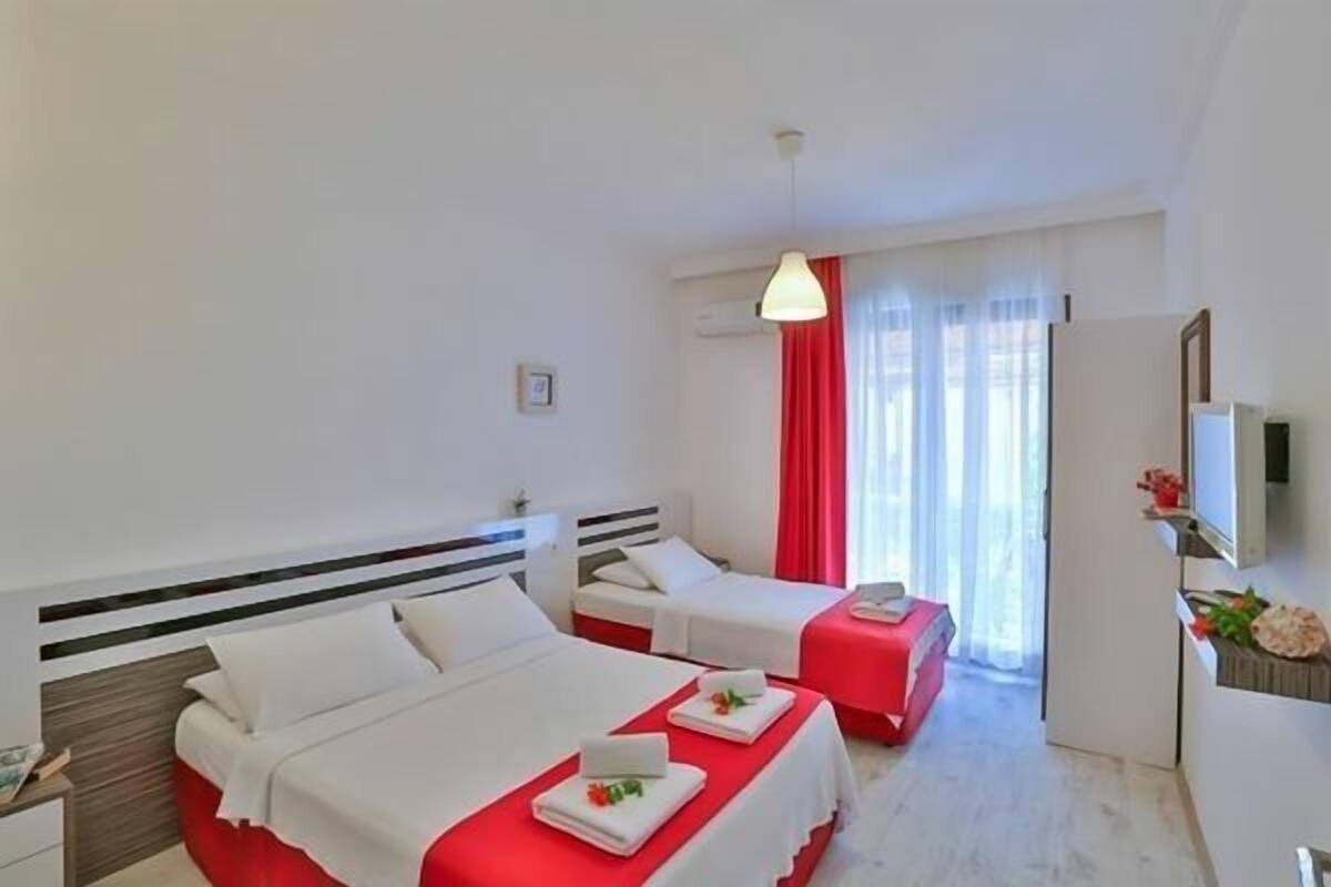 Una habitación de hotel con dos camas, una pared de acento roja, un escritorio pequeño y un espejo.