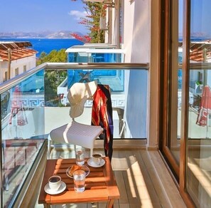 A balcony with a table set for two, a chair, and a view of the sea and buildings.