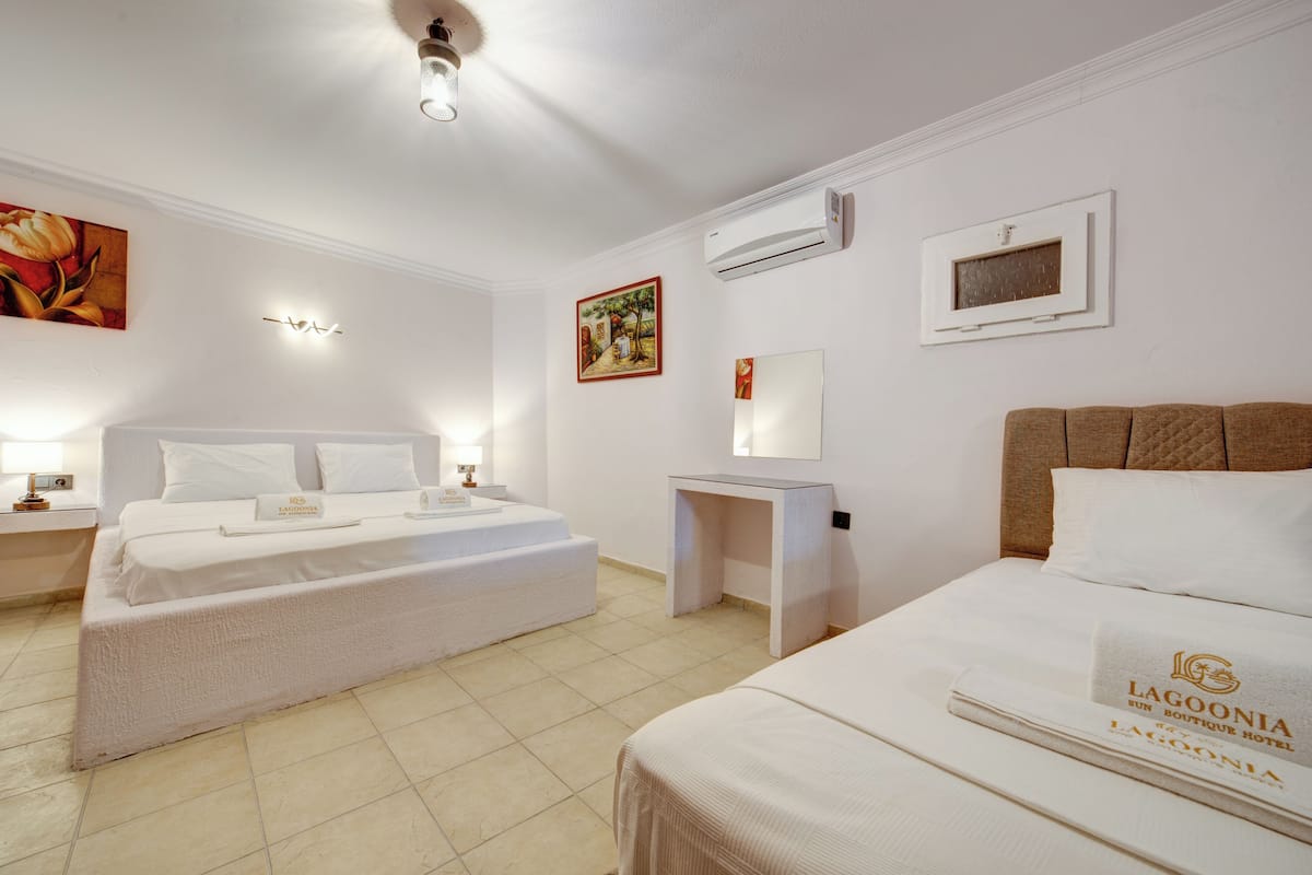 A hotel room with a bed, a bedside table, an air conditioning unit, and a wall-mounted artwork.