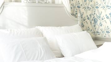 Un letto con lenzuola e cuscini bianchi, una finestra con tende leggere e una parete a motivi floreali.