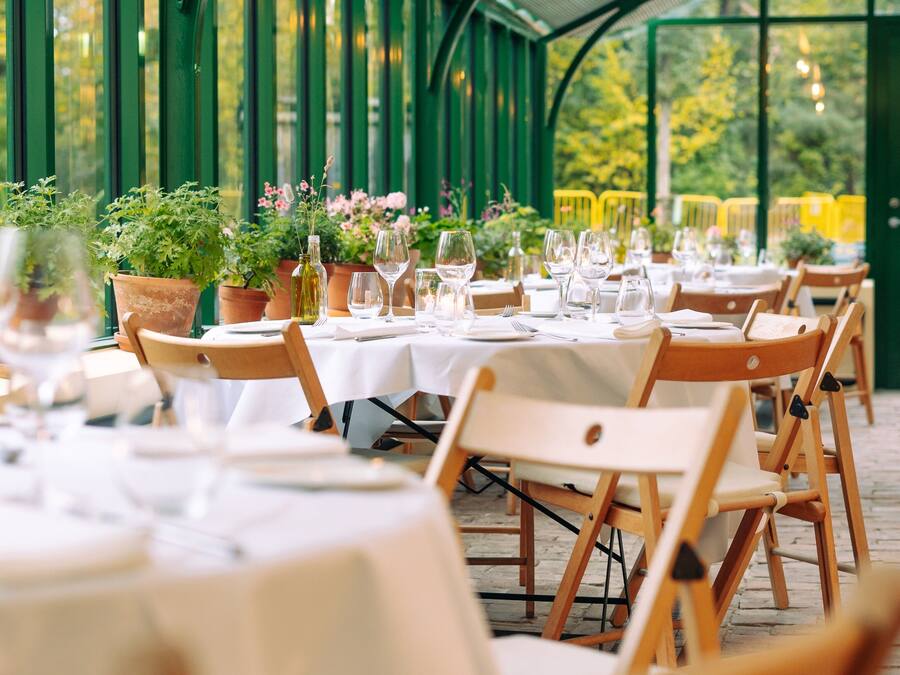 Een overdekte buitenruimte met eettafels, omgeven door groene metalen hekken en plantenpotten.
