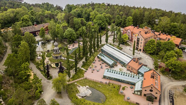 A hotel with a traditional European architectural style, featuring a central courtyard with a pond, surrounded by lush greenery and a view of a lake. - Ramme Fjordhotell - Unike Hoteller (Vestby)