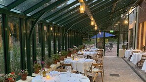 A covered outdoor dining area with tables set for a meal, surrounded by potted plants and a brick floor. - Ramme Fjordhotell - Unike Hoteller (Vestby)