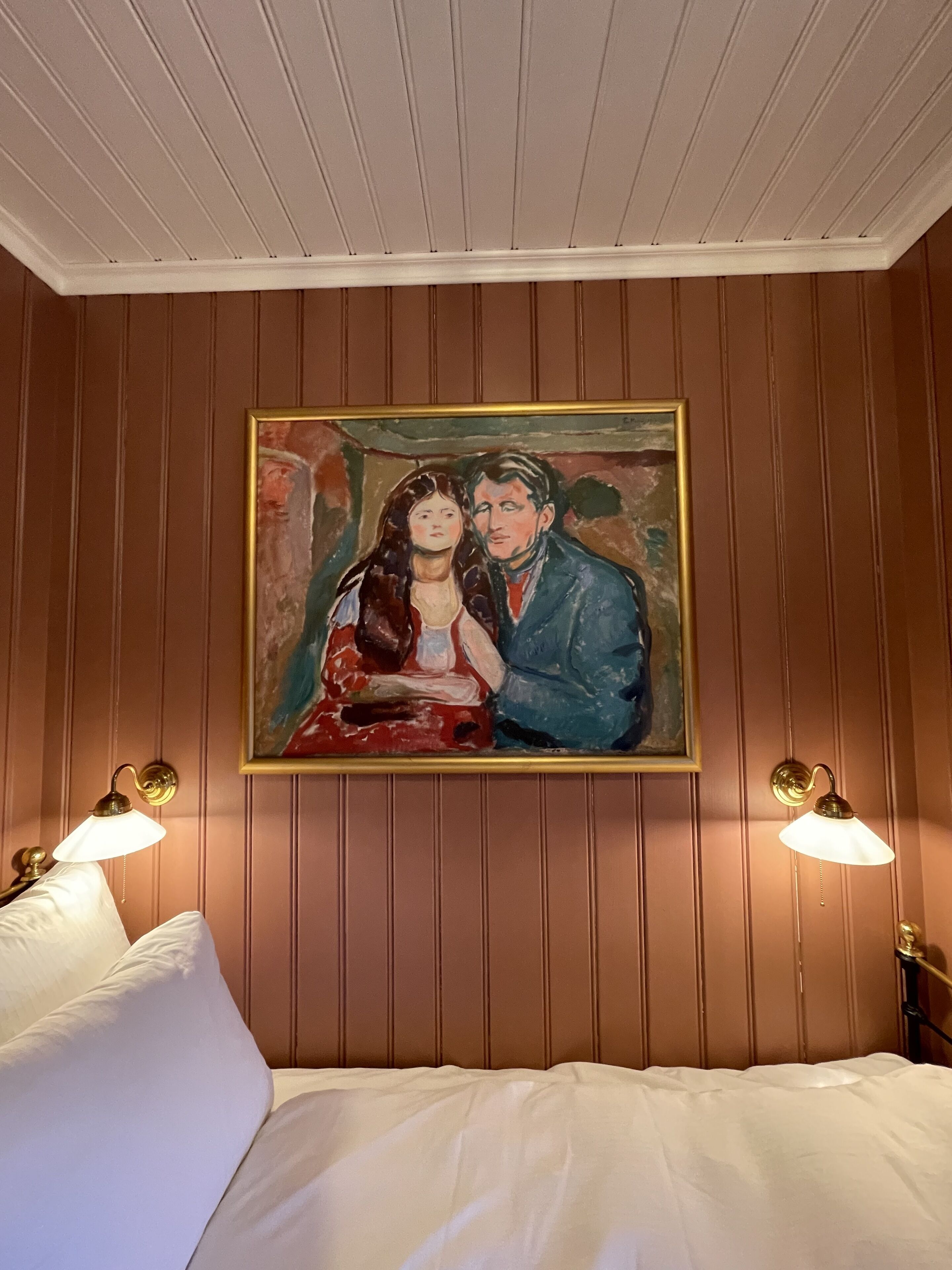 Une chambre à coucher avec un lit, deux lampes fixées au mur et un tableau au-dessus du lit.