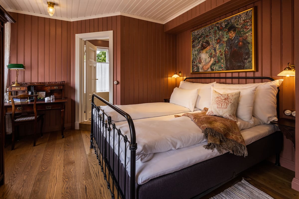A bedroom with a bed, a desk, and a painting on the wall.