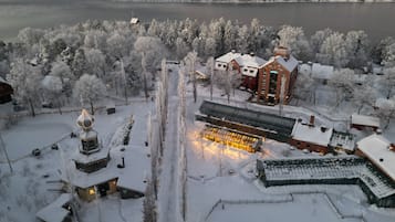 Un hotel con un edificio principale e un corpo secondario più piccolo, circondato da alberi innevati e un lago sullo sfondo.