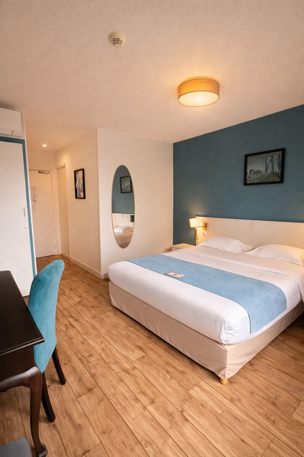 Une chambre d’hôtel équipée d’un lit, d’un bureau, d’une chaise, d’un miroir et d’un tableau accroché au mur.