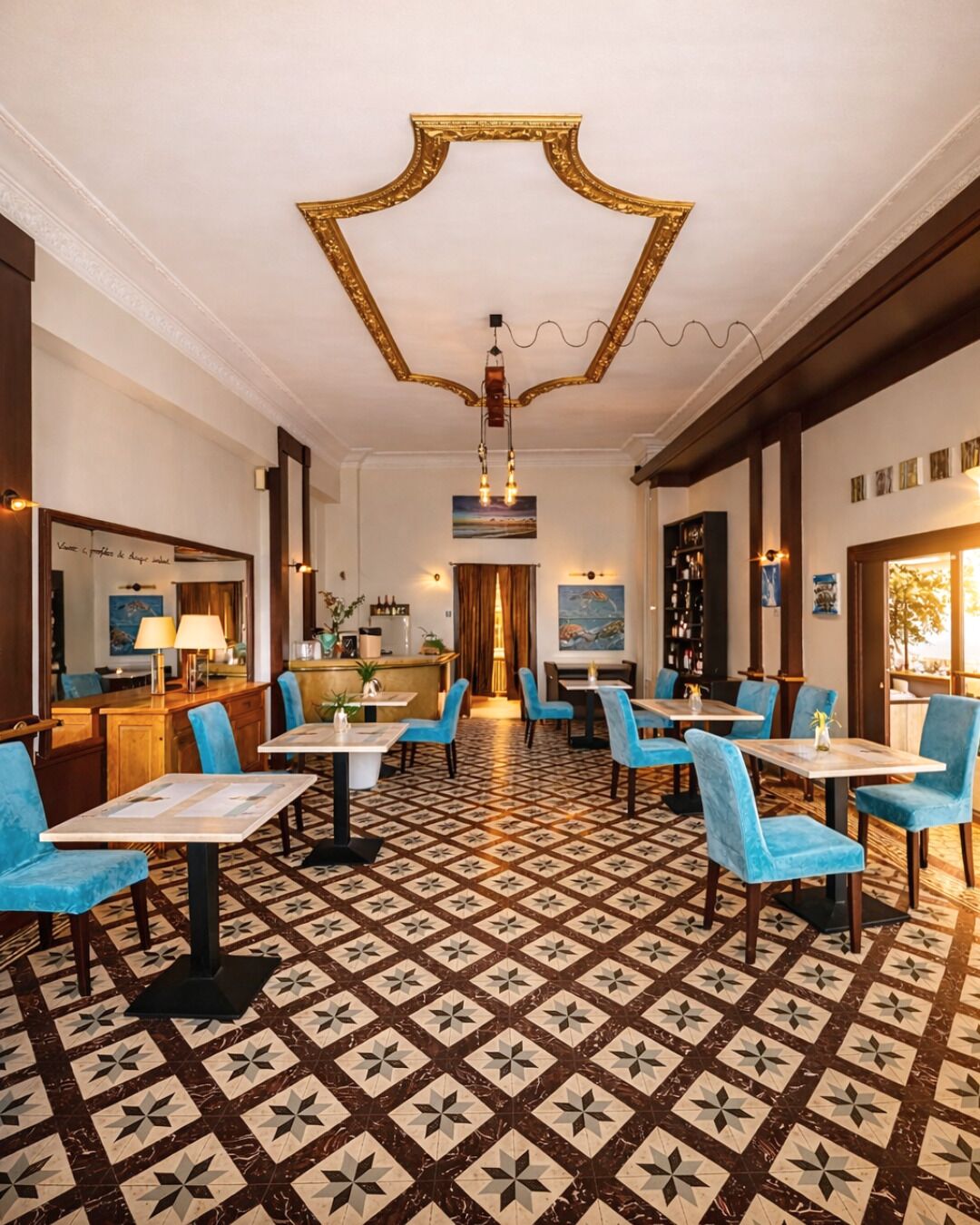 A hotel lobby with a patterned floor, blue chairs, and a central chandelier.