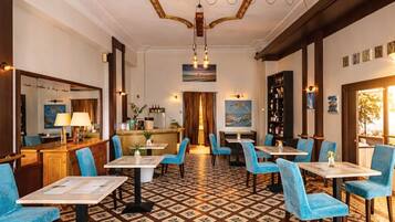 A hotel lobby with a patterned floor, blue chairs, and a central chandelier.