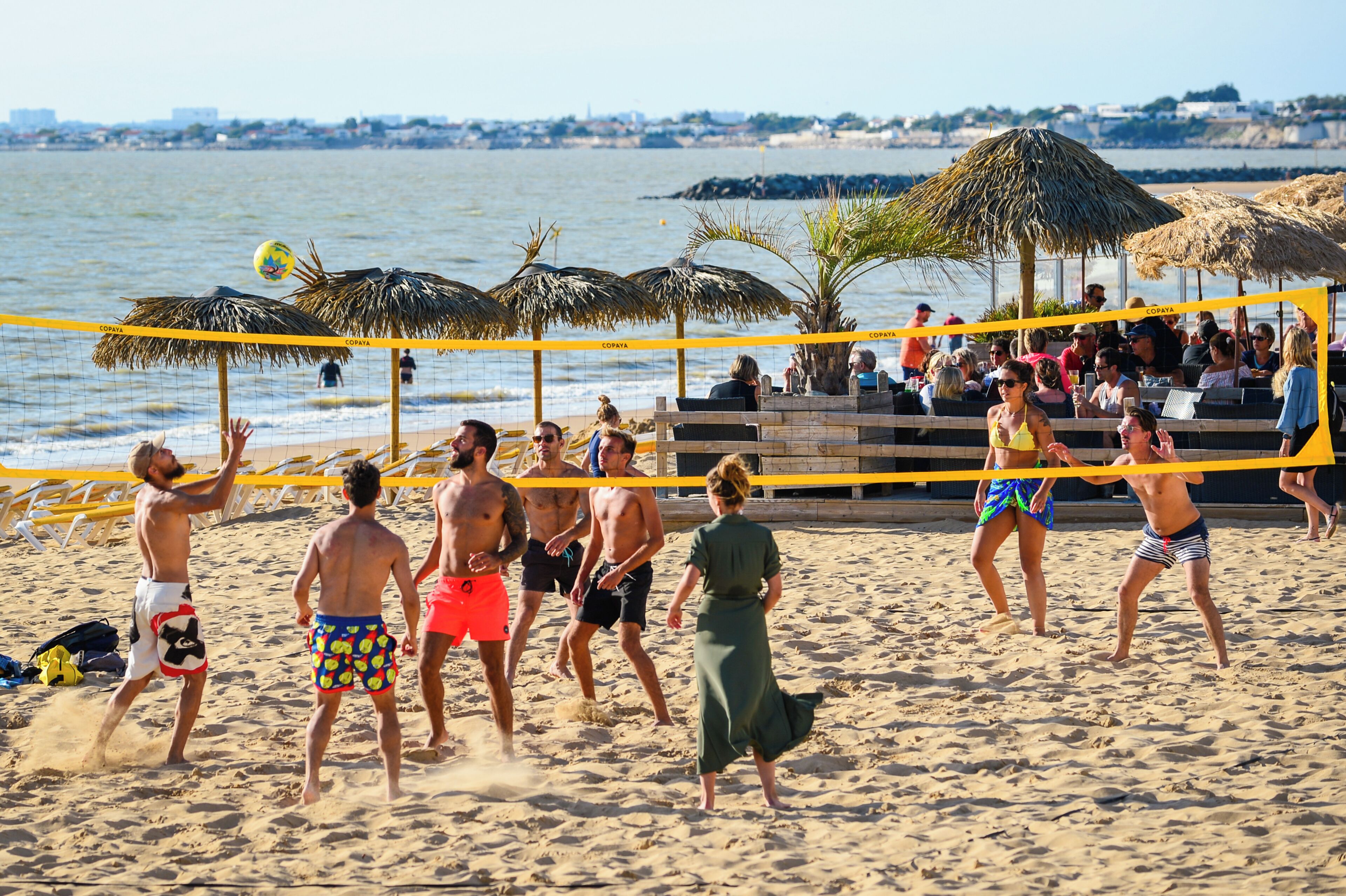 Partido de voleibol de playa con una red, espectadores y sombrillas.