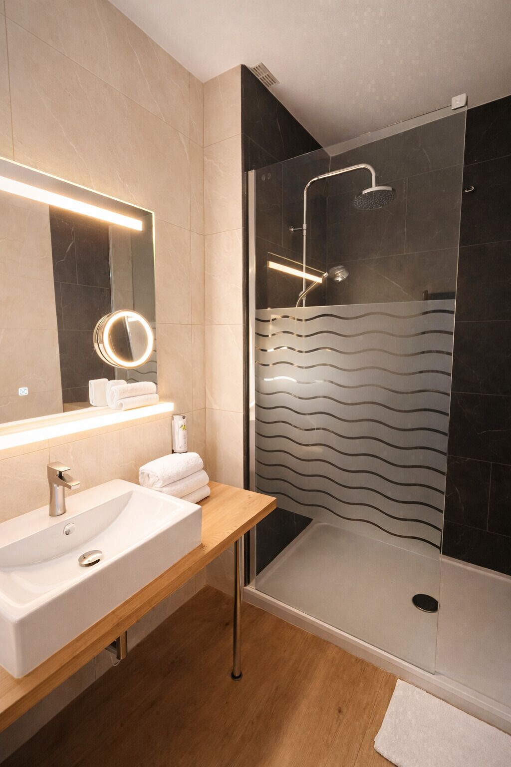 Un baño moderno con ducha de vidrio, tocador de madera con lavabo y espejo con luz.