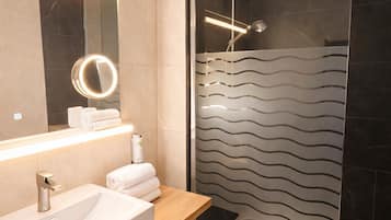 Un baño moderno con ducha de vidrio, tocador de madera con lavabo y espejo con luz.