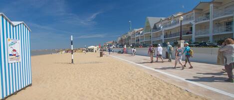 A beachside promenade with a handipage, a row of buildings with balconies, and people walking.