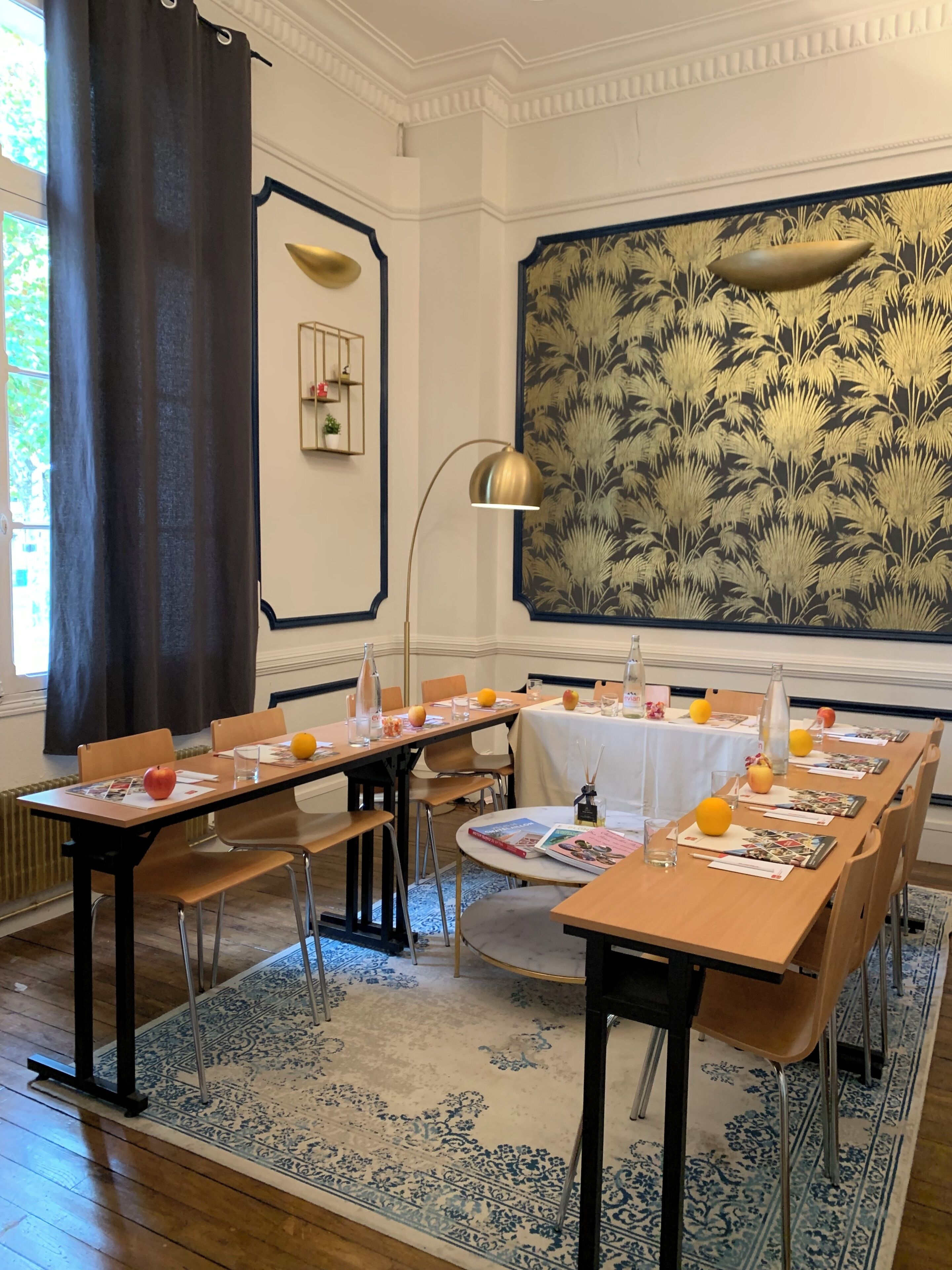 Un comedor con mesas dispuestas para una comida, un amplio muro decorativo y una ventana con cortinas.