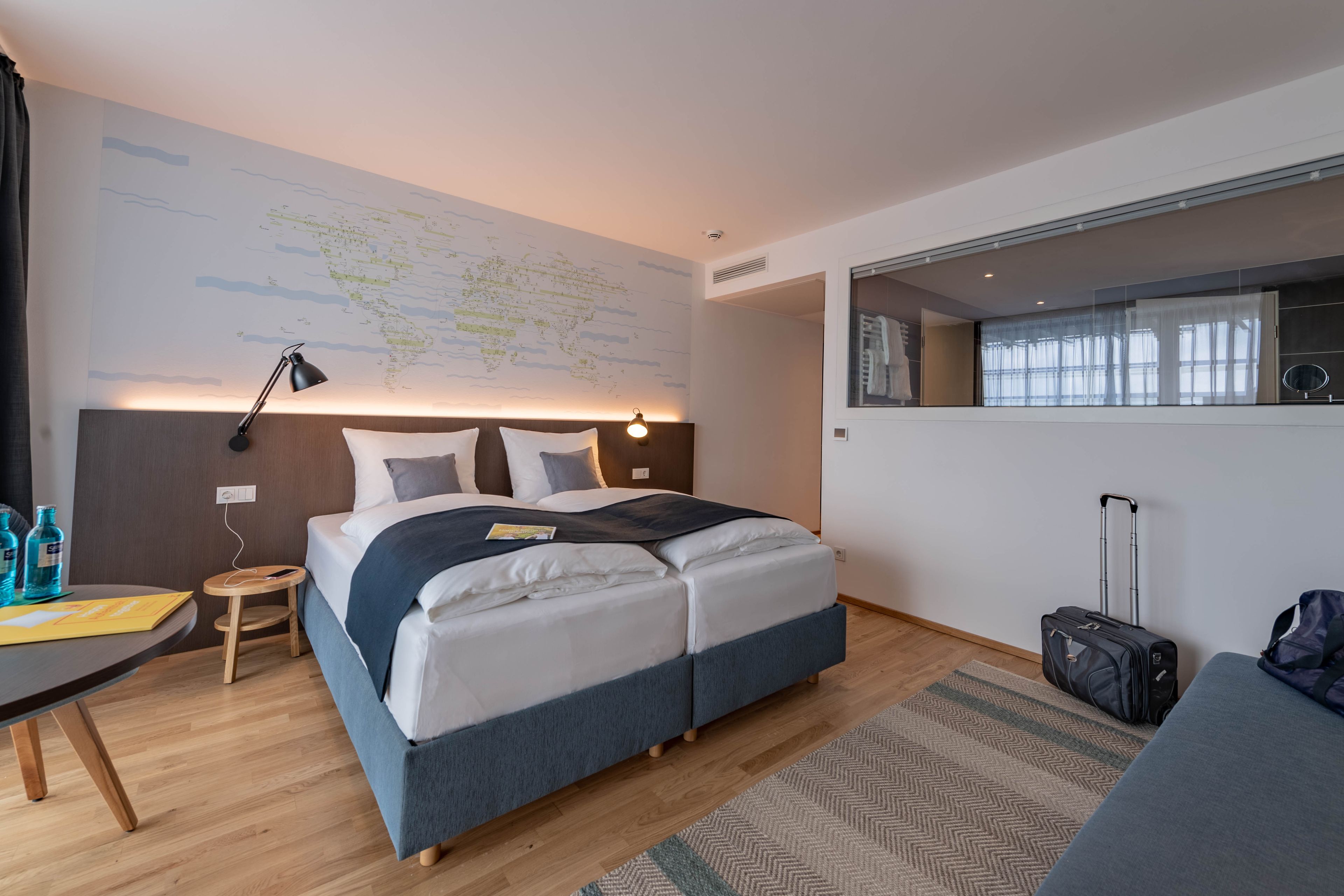 Une chambre d’hôtel moderne, dotée d’un grand lit, d’un bureau, d’une carte accrochée au mur et offrant une vue sur la ville par la fenêtre.