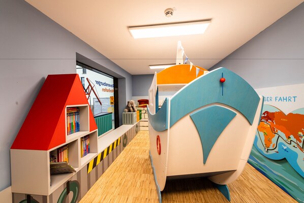 A children's play area with a bookshelf, a small house, and a boat-shaped play structure. - JUFA Hotel Hamburg HafenCity (Hamburg)