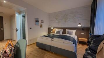 A hotel room with a bed, a desk, a chair, a map on the wall, and a suitcase.