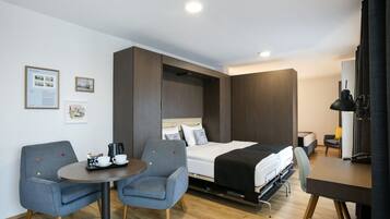 Una habitación de hotel compacta con cama, escritorio, dos sillas, una mesita y estación de café.