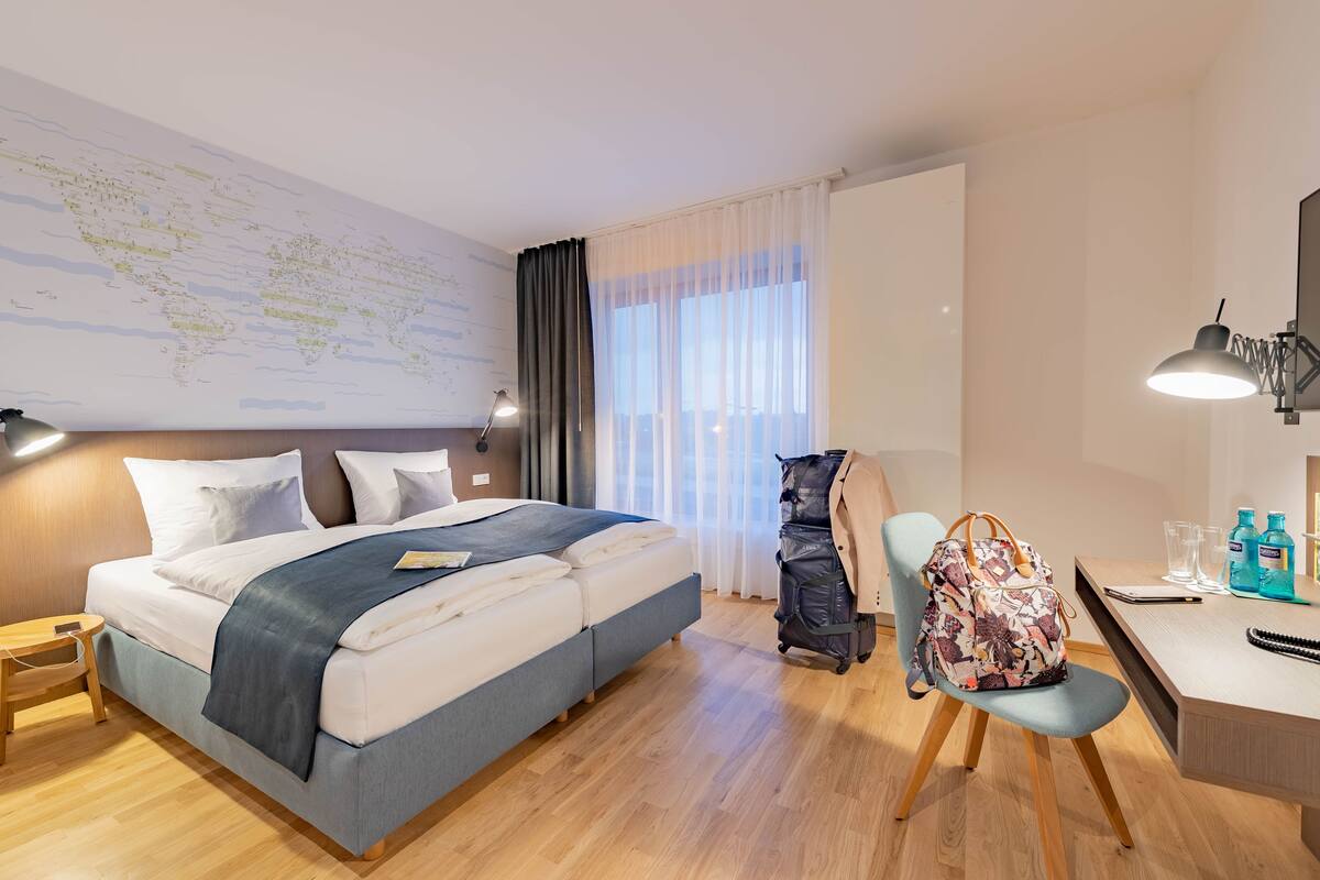 Una camera d'albergo con un letto, una scrivania, una sedia e una mappa appesa al muro.