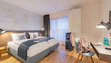 A hotel room with a bed, desk, chair, and a map on the wall.