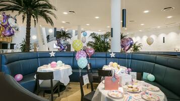 Un ristorante con una zona salotto in blu, tavoli bianchi e diversi palloncini.