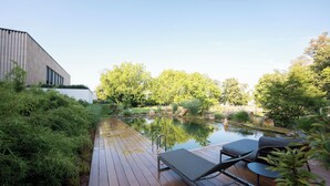 A wooden deck with a pool, lounge chairs, and a modern building in the background.