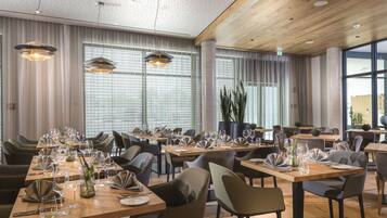 A modern dining area with multiple tables set for dining, featuring contemporary chairs and pendant lighting.