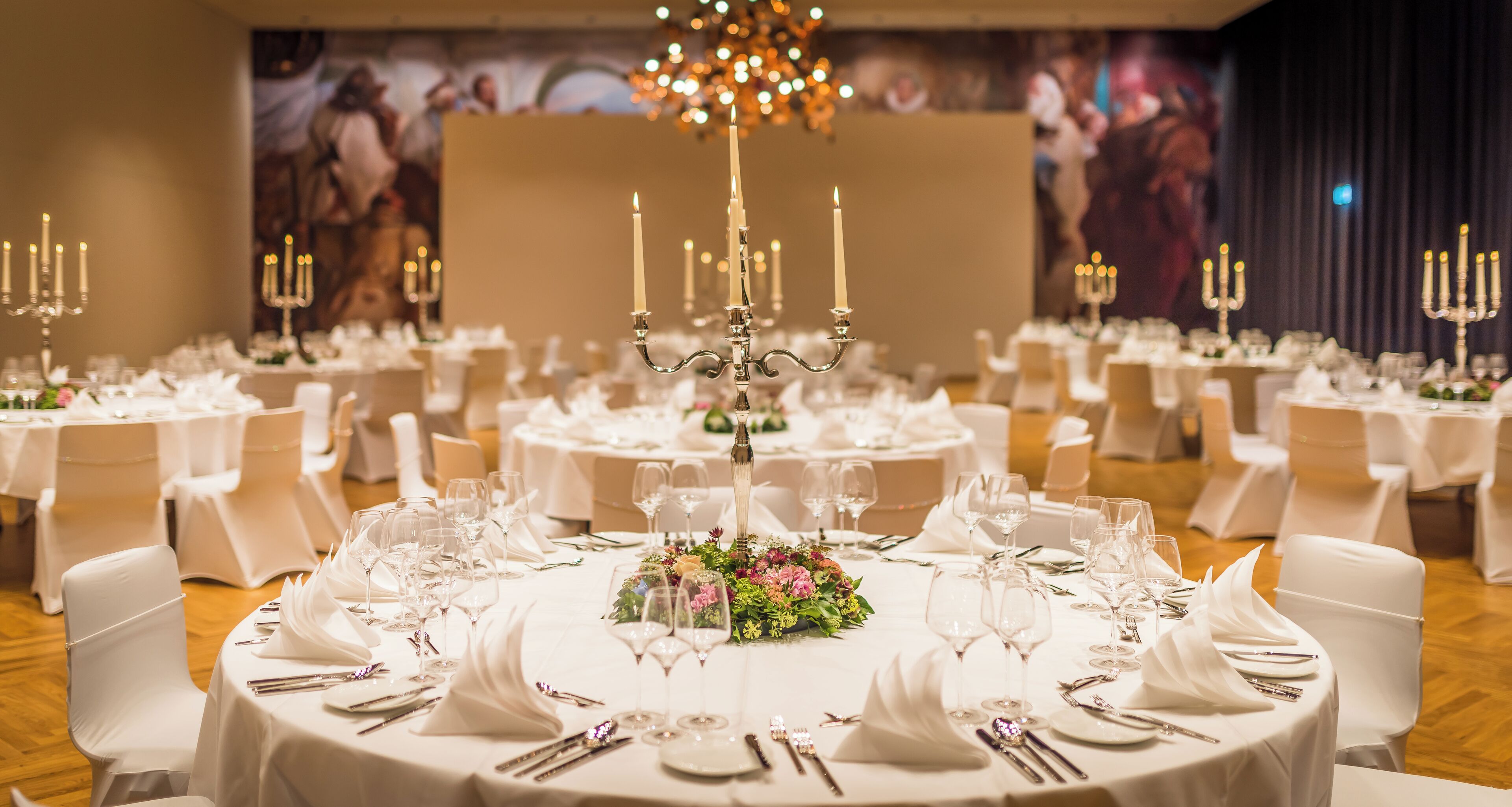A banquet hall with round tables, white tablecloths, and candle centerpieces.