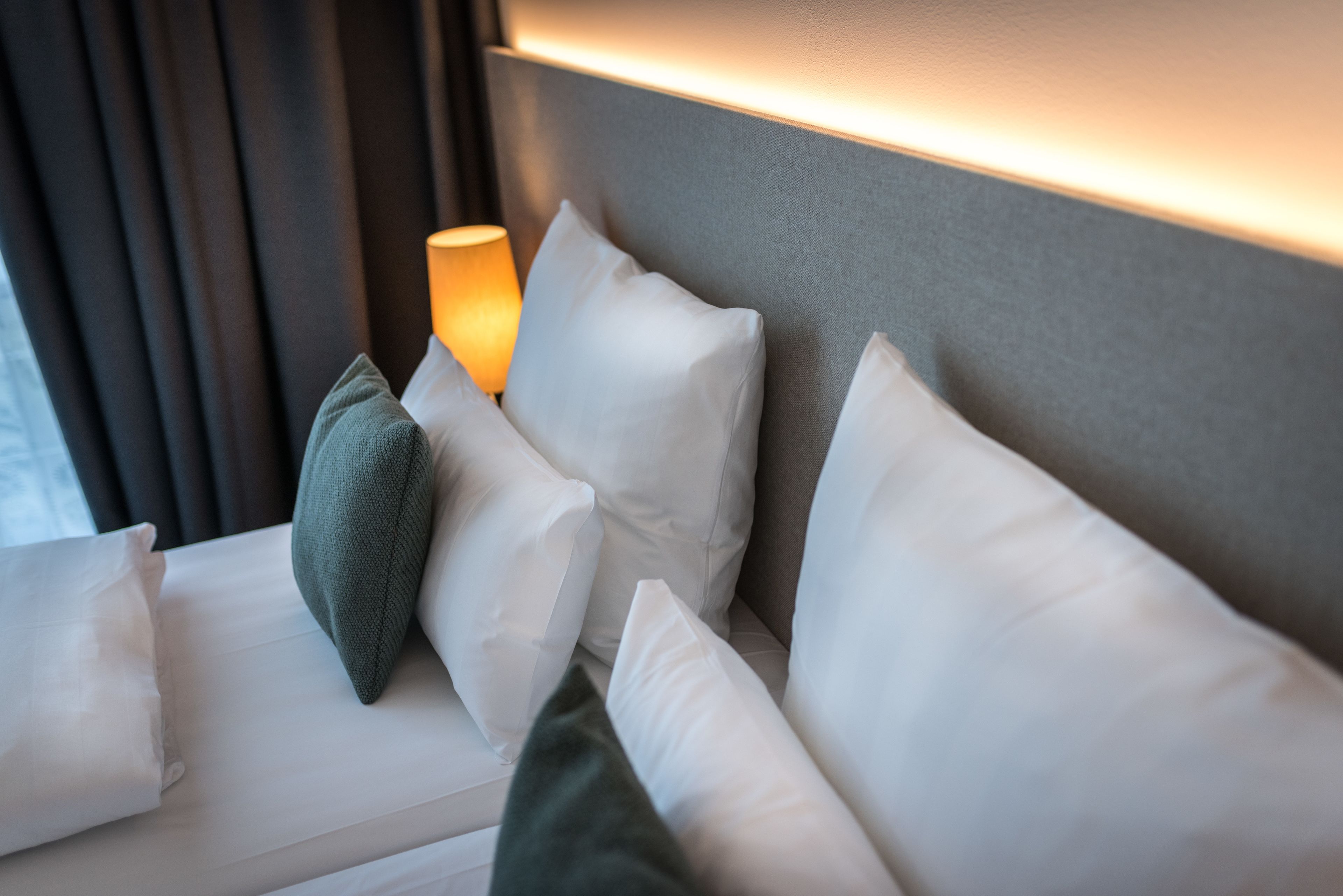 Ein ordentlich gemachtes Bett mit weißen und grünen Kissen, einer Nachttischlampe und einem Kopfteil mit LED-Beleuchtung.