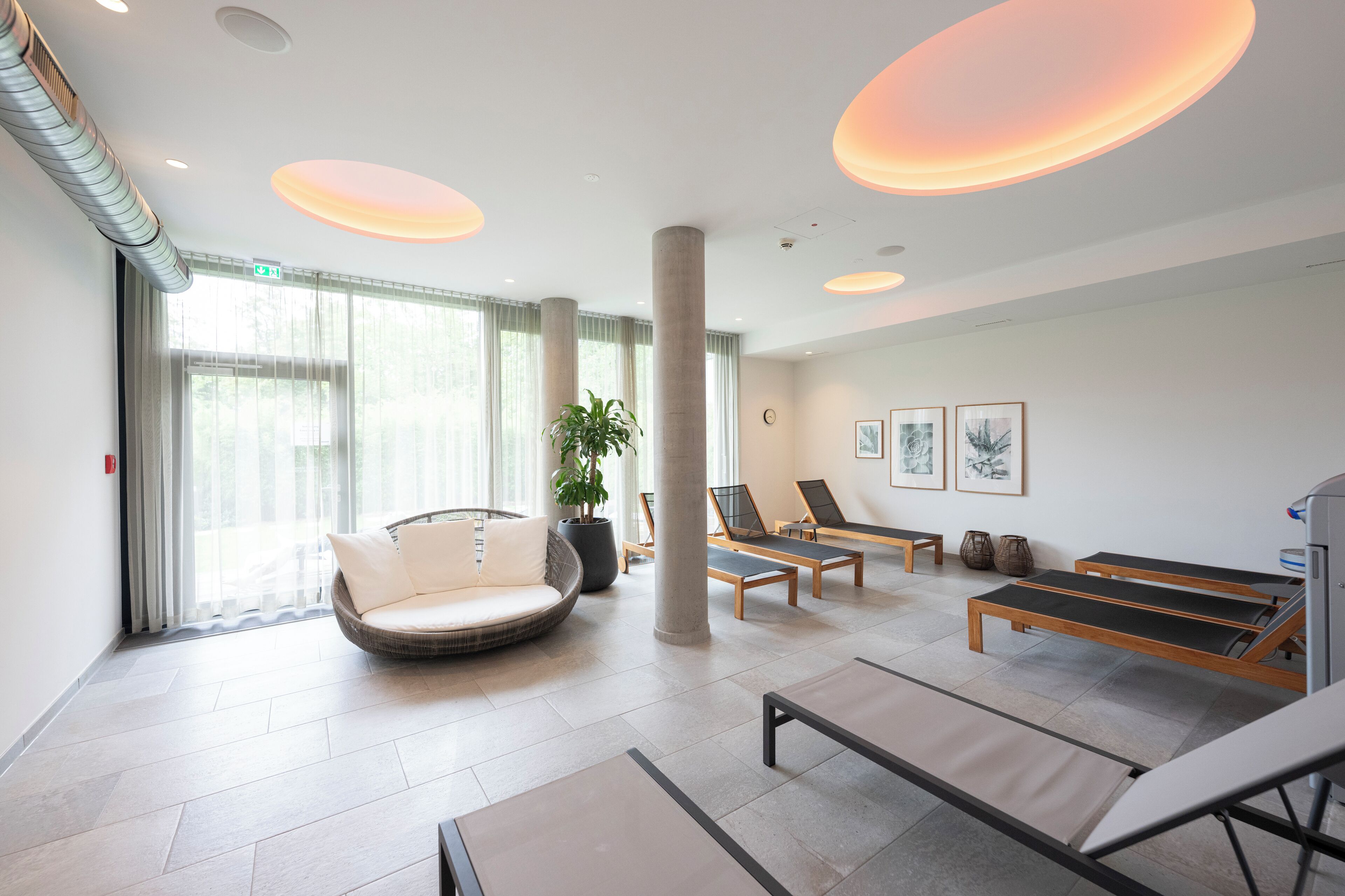 Um spa moderno com uma janela grande, uma área de estar circular e vários espreguiçadeiras.