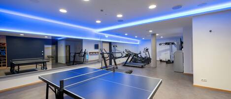 Un gimnasio con equipo de ejercicio, una mesa de ping pong y una cinta de correr.