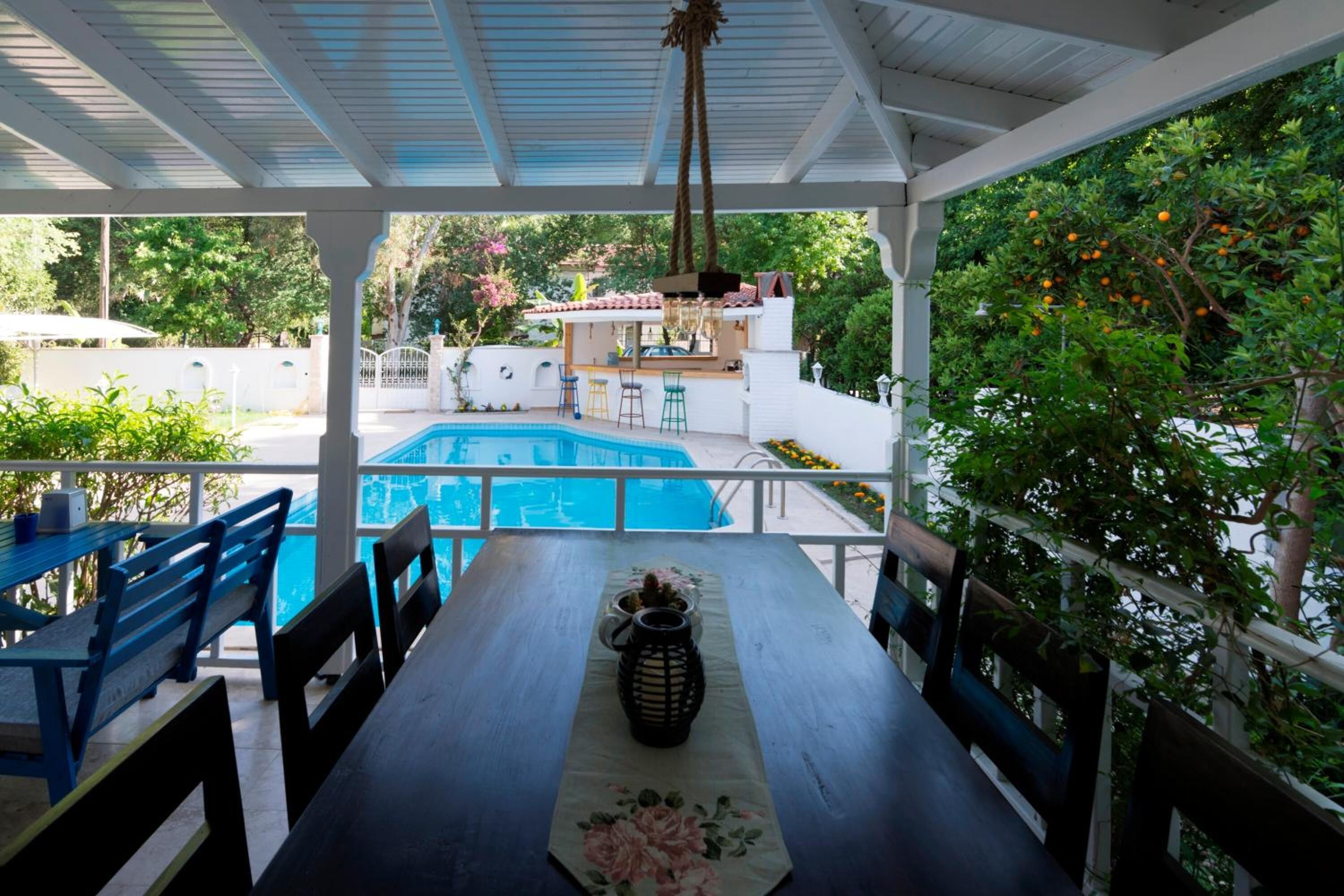 A covered outdoor area with a pool, a dining table with chairs, and a bar area with stools.