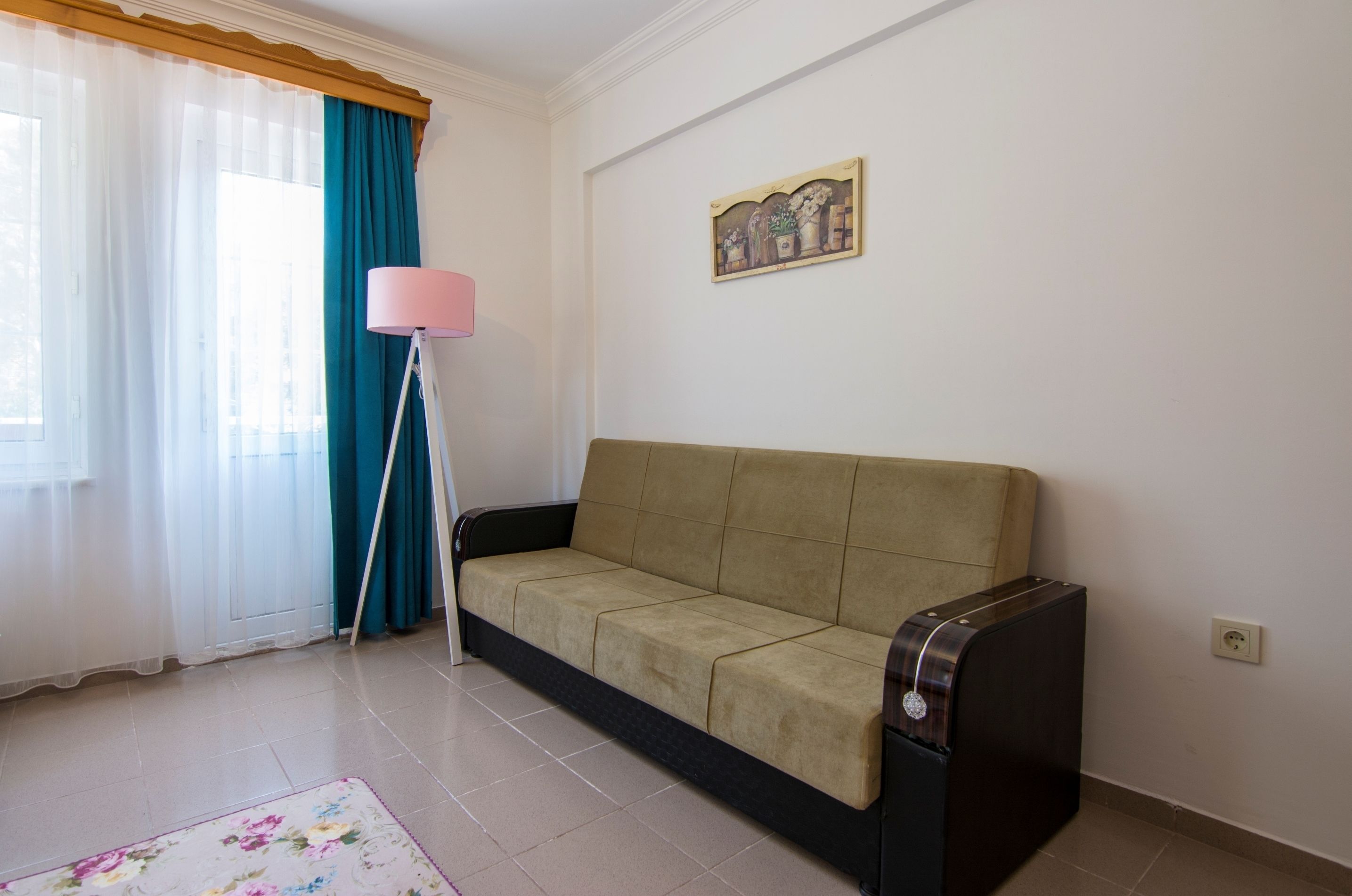 Ein Zimmer mit einem beigen Sofa, einer pinkfarbenen Stehlampe, einem floralen Teppich und einem Gemälde an der Wand.