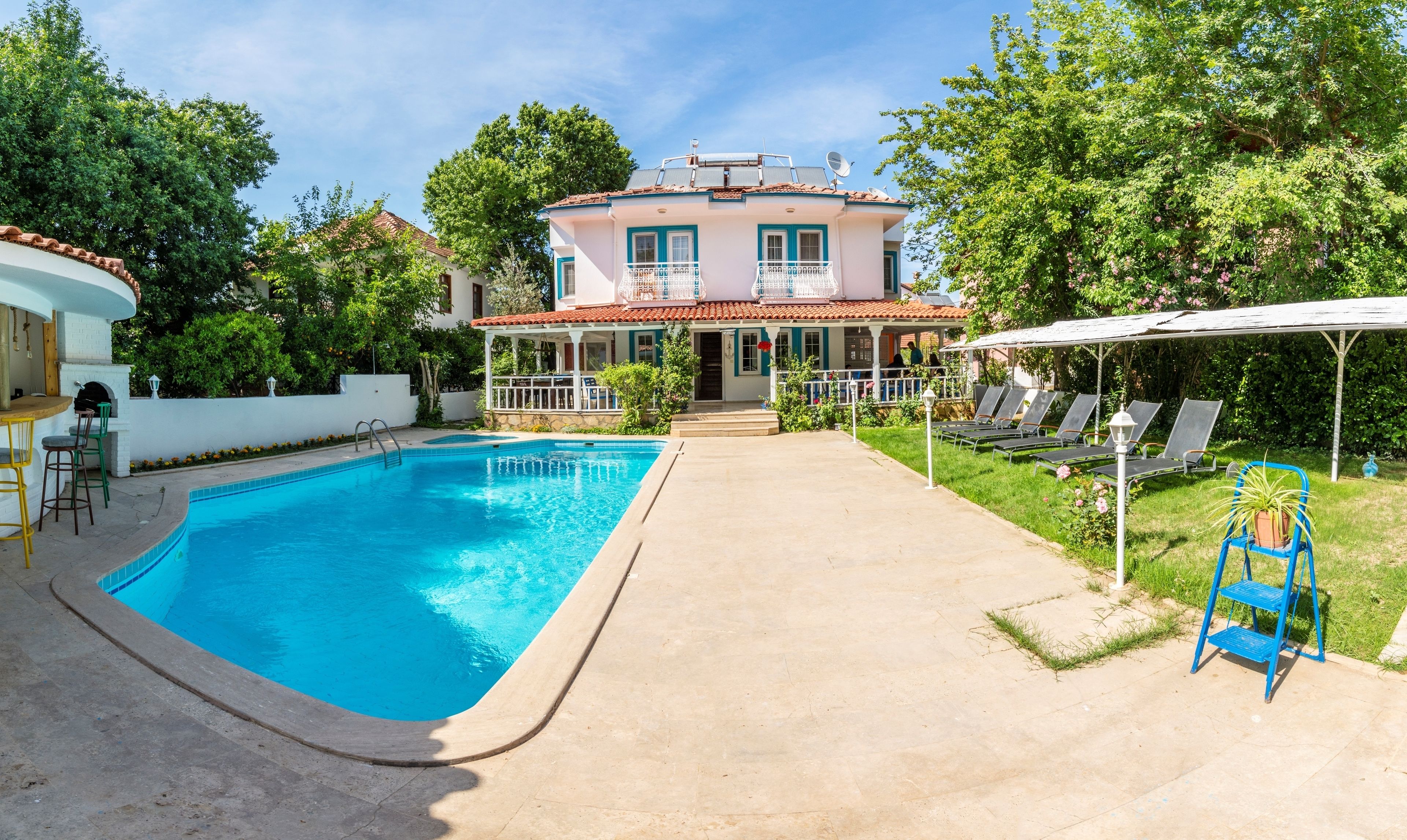 Una casa de dos plantas con piscina, un porche cubierto y un jardín.