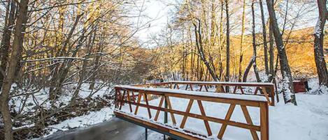 A wooden bench with snow on it, surrounded by trees and a frozen stream.
