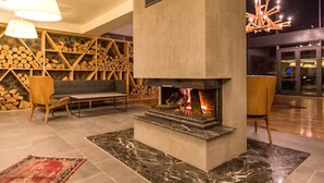 A cozy lounge area with a fireplace, wooden shelves, comfortable seating, and a modern chandelier. - Abant Lotus Otel (Bolu)