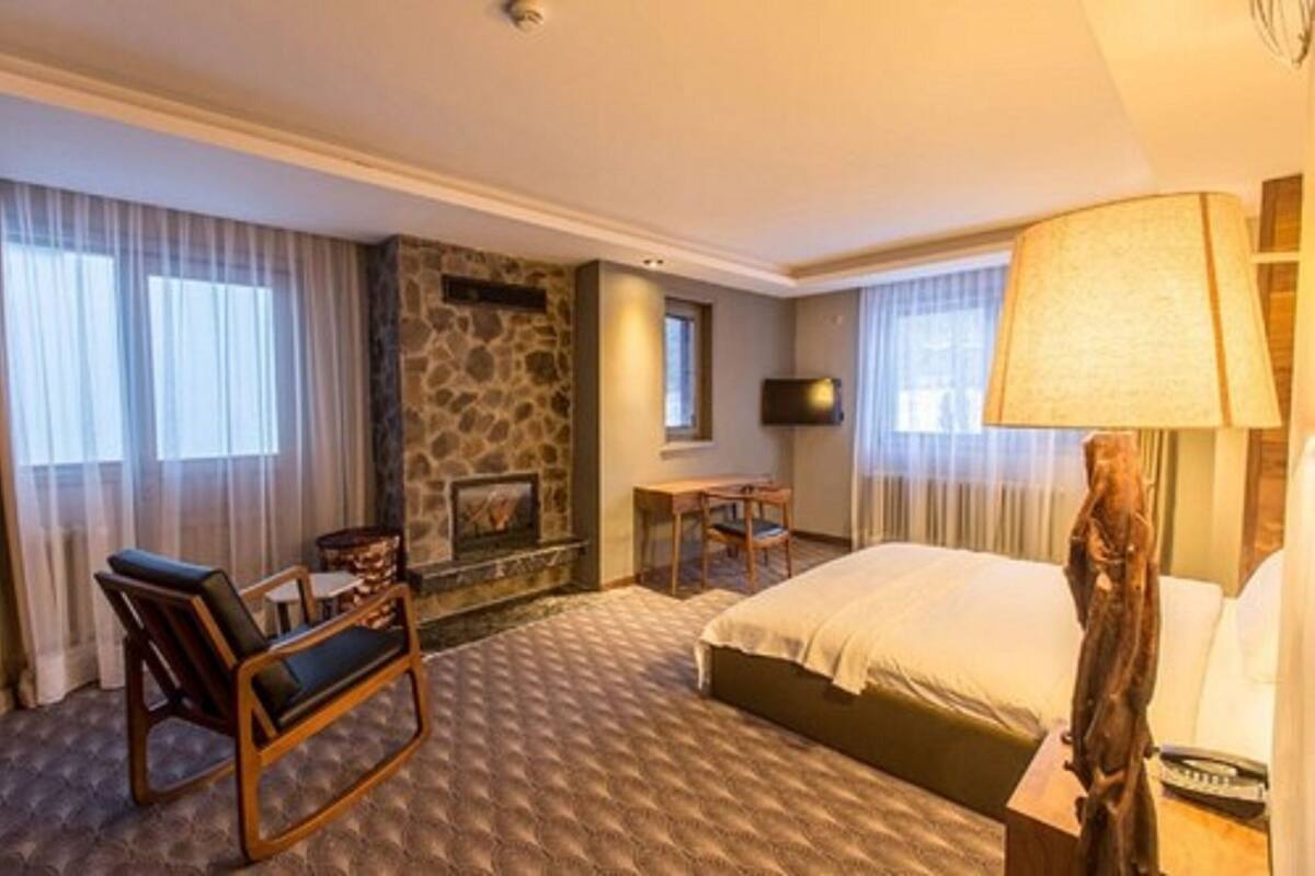 A hotel room with a bed, a desk, a chair, a stone fireplace, and a television.