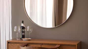 A wooden desk with a round mirror, two wine glasses, and a bottle of wine.