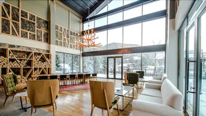 A spacious living area with a high ceiling, wooden flooring, and a large window offering a view of the outdoors. There are several seating options including a white sofa and two wooden chairs. - Abant Lotus Otel (Bolu)