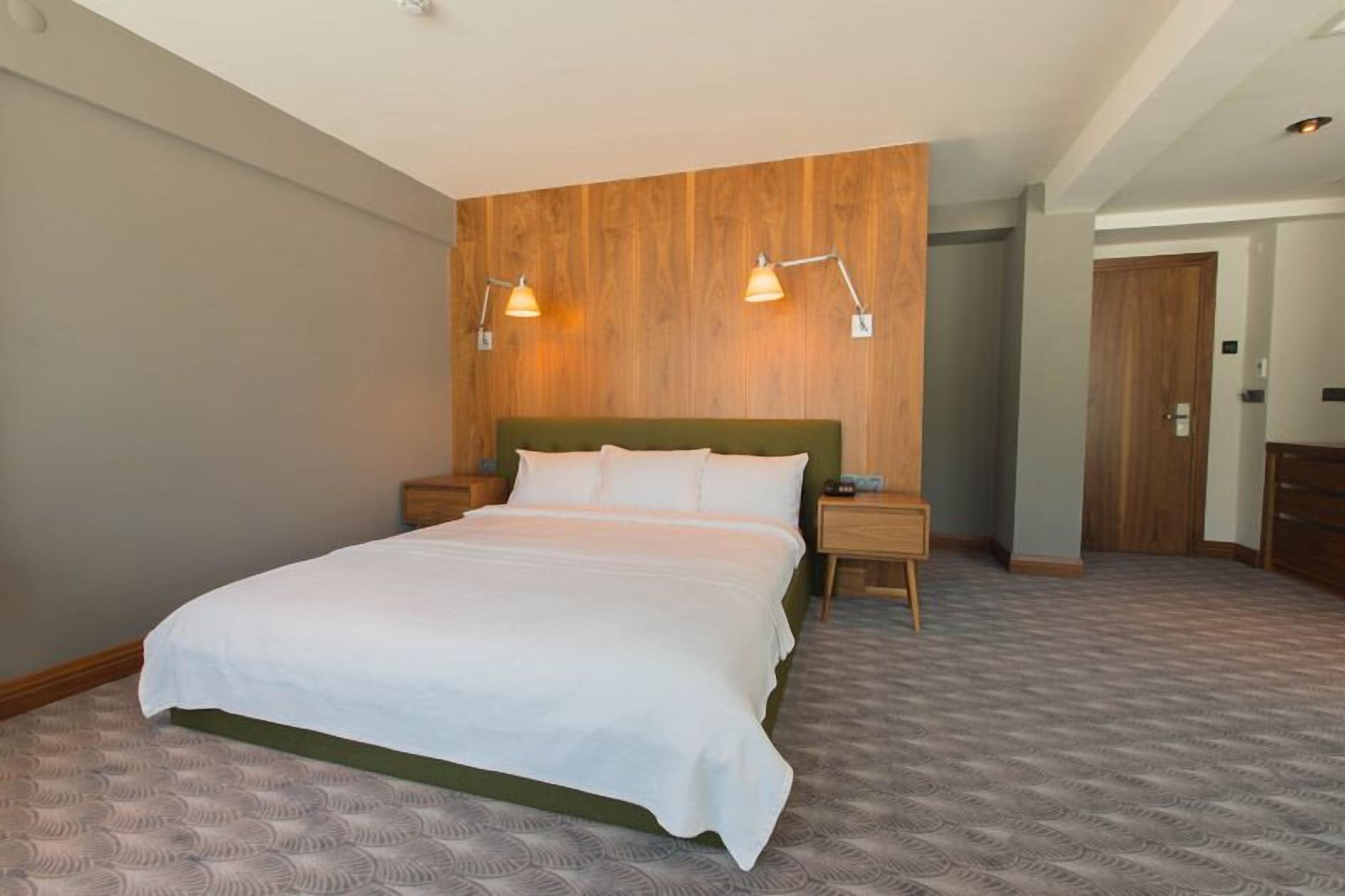 A hotel room with a large bed, wooden headboard, two bedside tables, and a nightstand.