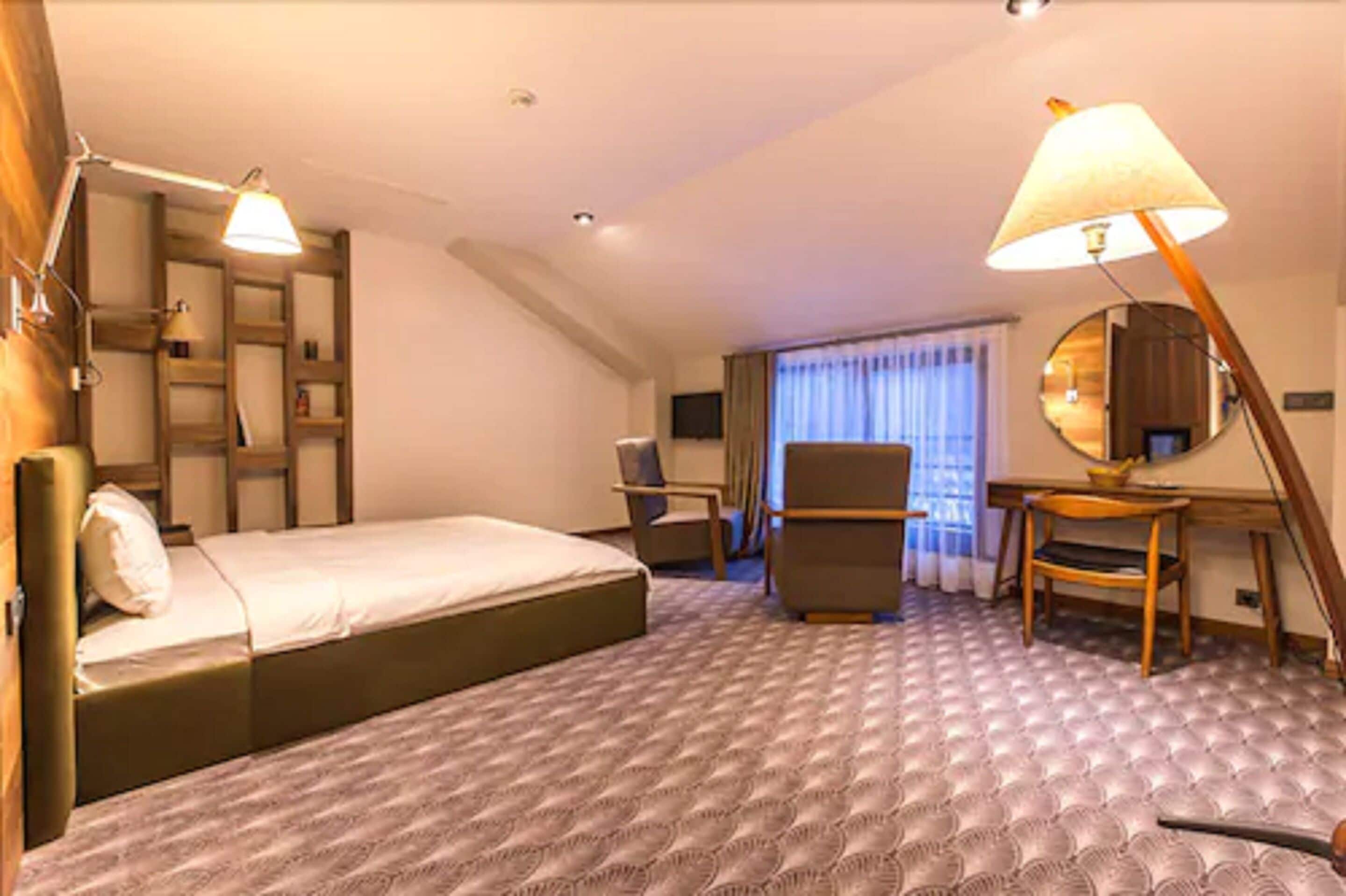A hotel room with a bed, a desk, a chair, a lamp, and a large mirror.