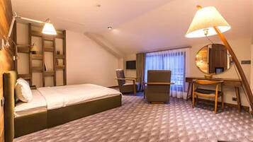 A hotel room with a bed, a desk, a chair, a lamp, and a large mirror.