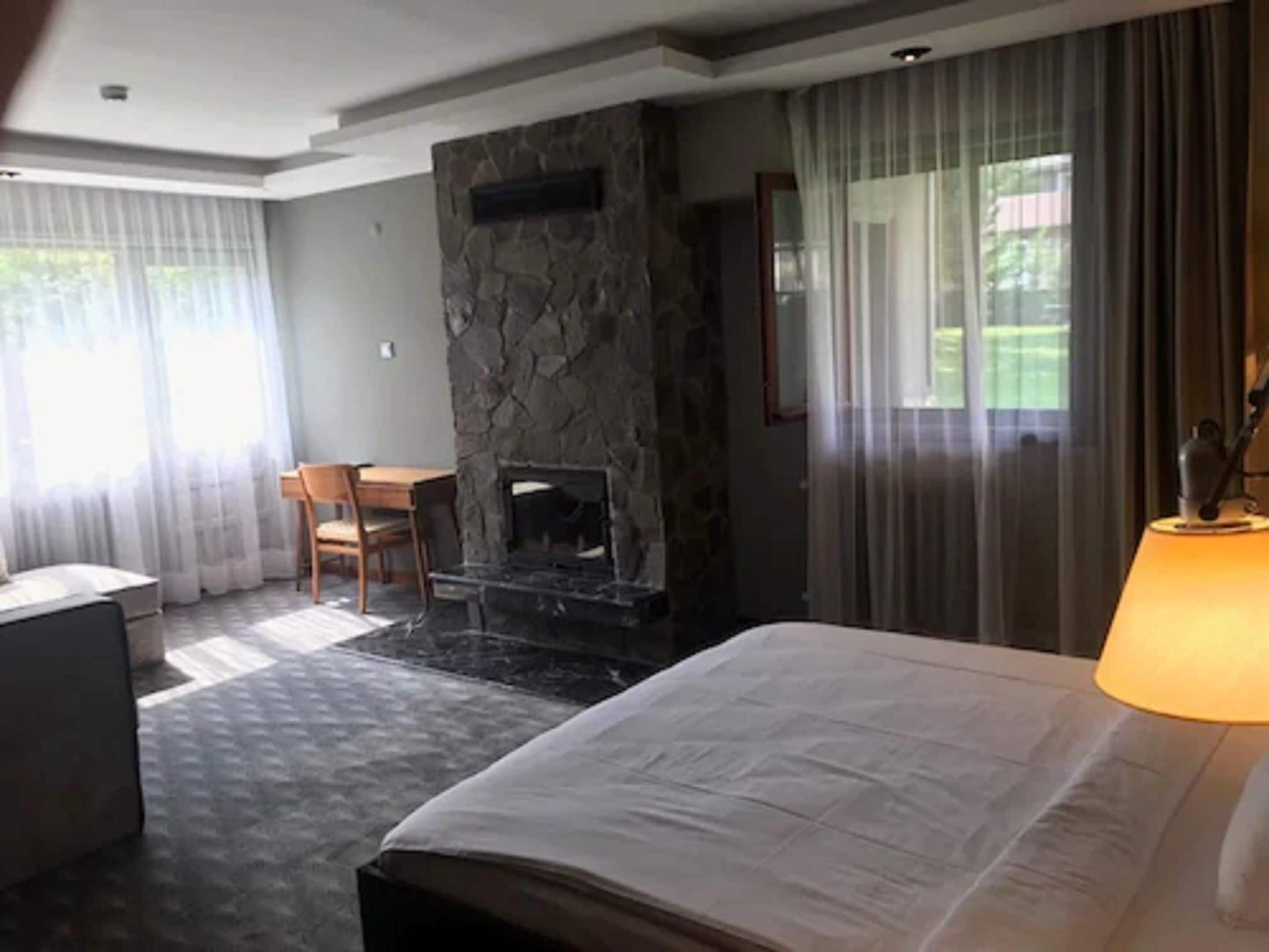 A hotel room with a stone fireplace, a bed, a desk, and a chair.