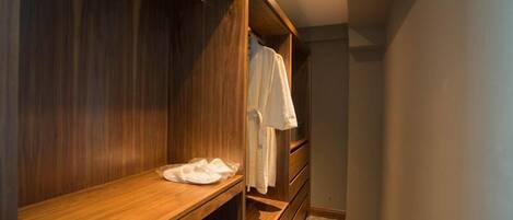 A walk-in closet with wooden shelving and a bench, featuring a hanging robe and a folded white towel.