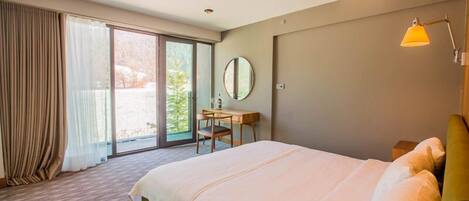 Quarto de hotel com uma cama grande, uma escrivaninha, uma cadeira e vista através de uma porta de vidro deslizante.