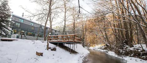 A snow-covered path leading to a building with a wooden bridge over a stream.