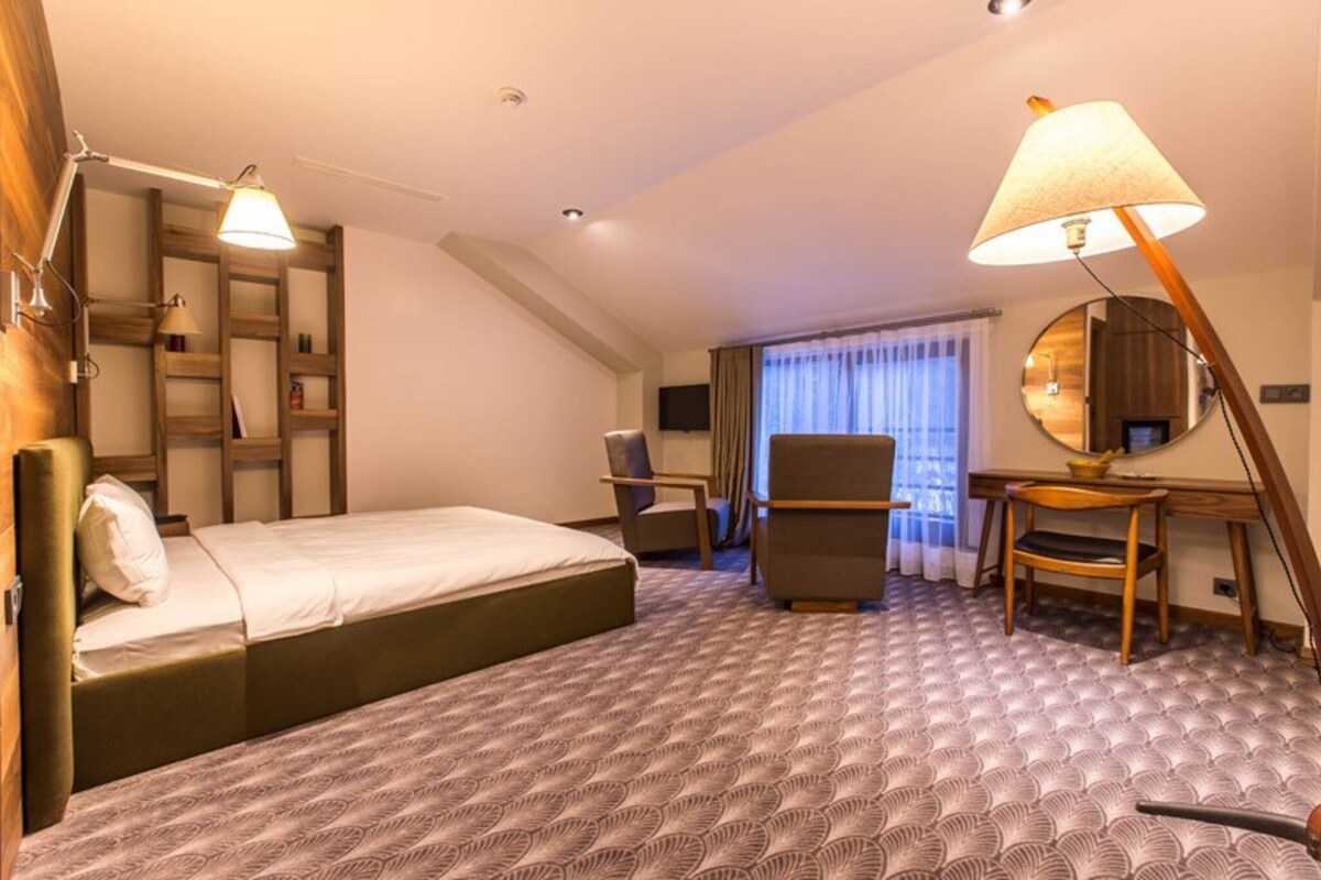 A hotel room with a bed, desk, chair, and a large mirror.