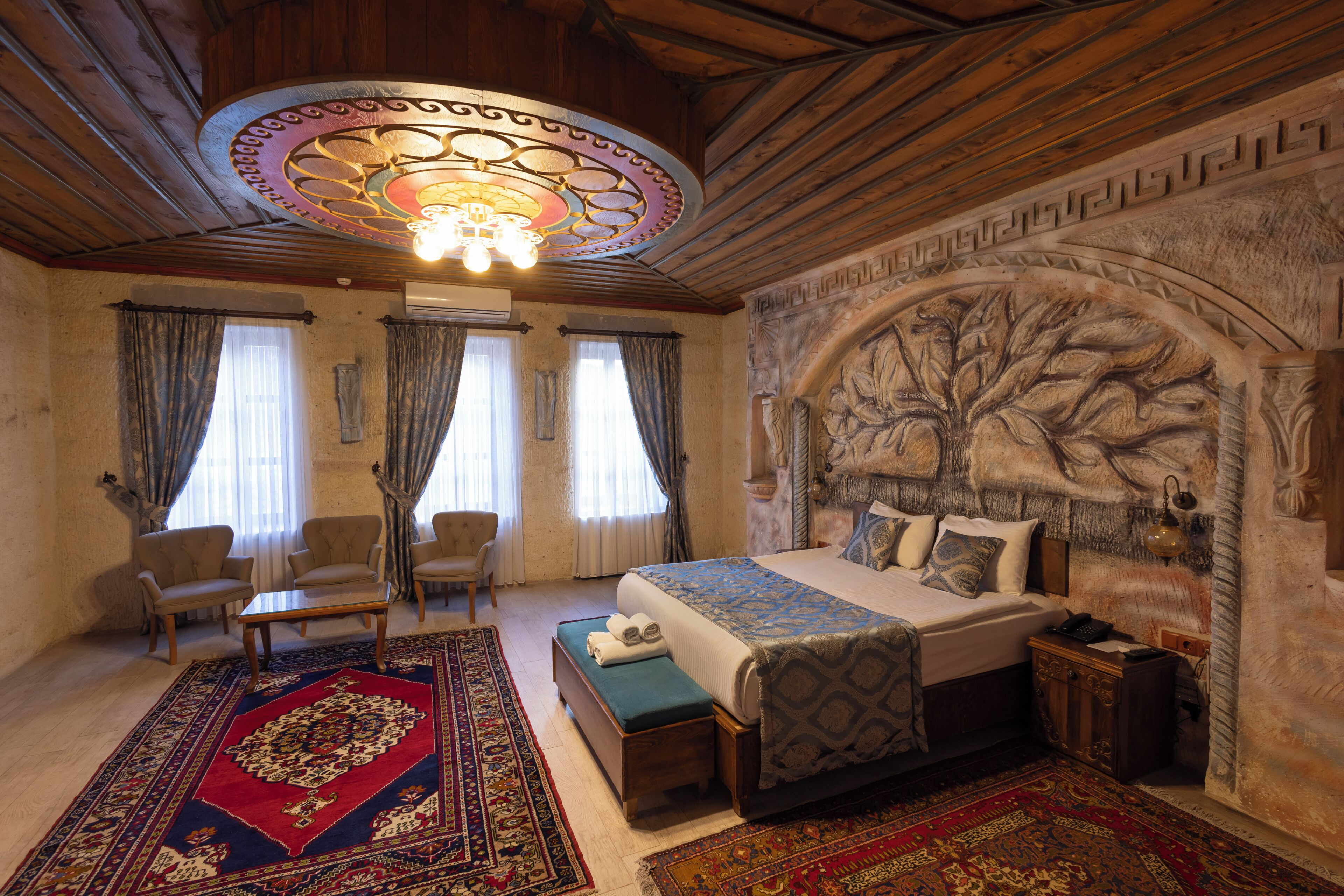 A bedroom with a large bed, two armchairs, a wooden ceiling, and a decorative wall.