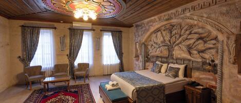 A bedroom with a large bed, two armchairs, a wooden ceiling, and a decorative wall.